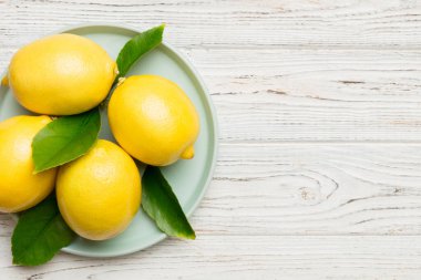Taze kesilmiş limon ve tüm limonları renkli arka planda yuvarlak tabakta. Yemek ve içecek malzemeleri hazırlanıyor. Sağlıklı beslenme teması üst görünüm kopyalama alanı.