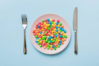 cutlery on table and sweet plate of candy. Health and obesity concept, top view on colored background.