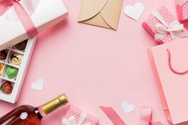 top view photo of st valentine day decor shopping, bag, wine, bottle, envelope, gift, box, candy and red heart on colored background with empty space. Frame background.