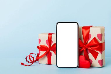 mobile phone with blank screen on colored background with hearts, calendar and gift box, valentine day concept perspertive view flat lay.