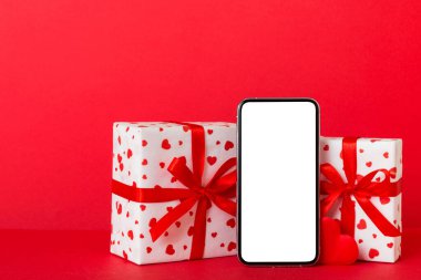 mobile phone with blank screen on colored background with hearts, calendar and gift box, valentine day concept perspertive view flat lay.