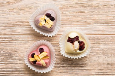 chocolate sweets in the form of a heart with fruits and nuts on a colored background. top view with space for text, holiday concept.