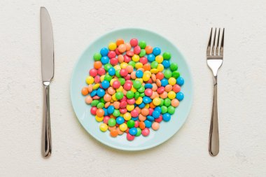 cutlery on table and sweet plate of candy. Health and obesity concept, top view on colored background.