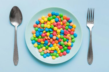 cutlery on table and sweet plate of candy. Health and obesity concept, top view on colored background.