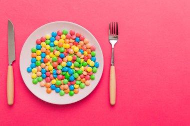 cutlery on table and sweet plate of candy. Health and obesity concept, top view on colored background.