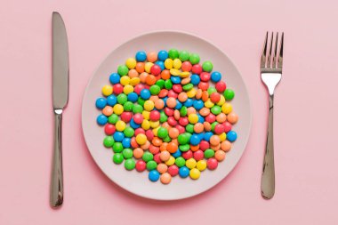 cutlery on table and sweet plate of candy. Health and obesity concept, top view on colored background.