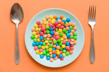 cutlery on table and sweet plate of candy. Health and obesity concept, top view on colored background.