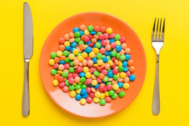 cutlery on table and sweet plate of candy. Health and obesity concept, top view on colored background.