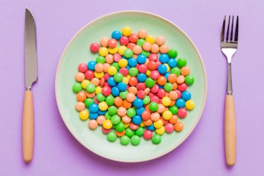 cutlery on table and sweet plate of candy. Health and obesity concept, top view on colored background.