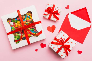 Red envelope with candy and gift box and Valentines hearts on colored background. Flat lay, top view. Romantic love letter for Holiday concept.