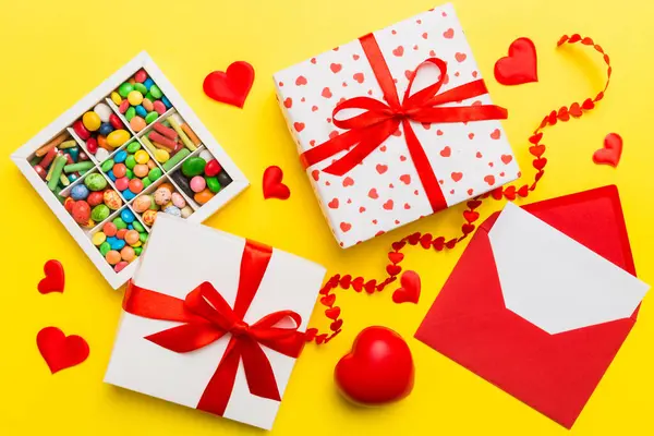 Red envelope with candy and gift box and Valentines hearts on colored background. Flat lay, top view. Romantic love letter for Holiday concept.