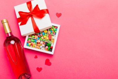 Sevgililer Günü için renkli arka planda bir şişe kırmızı şarap hediye ve çikolatalı. Kalp, hediye kutusuyla şekillendirilmiş çikolatalar fotokopi alanı ile üst görünüm.