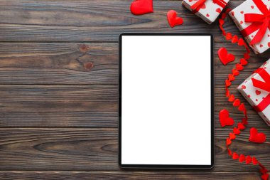 Top view of digital tablet with gift boxes and hearts on colorful background. Tablet with black screen with Holiday decorations gift box top view.