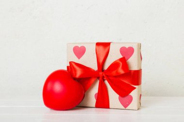 gift box with red bow and red heart on colored background. Perspective view. Flat lay.