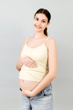 Gri arka planda hamilelik kemeri ve fotokopi alanı kullanan hamile bir kadının portresi. Ortopedik abdominal destek kemeri kavramı.