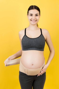 Üçüncü üç aylık dönemde hamilelik korsesi giyen hamile kadının portresi sarı arka planda fotokopi alanı ile. Ortopedik abdominal destek kemeri kavramı.