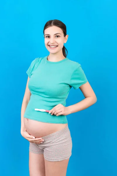 positive pregnancy test with two stripes against happy pregnant woman abdomen at Colored background. Future mother in gray dress. Pregnancy surprise. Copy space.