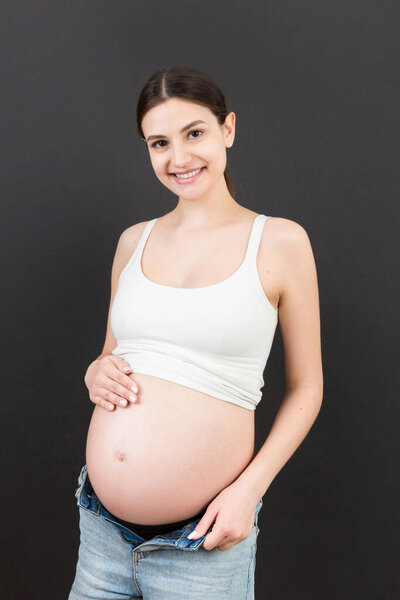 pregnant belly at colorful background with copy space. Expecting mother in opened jeans. Motherhood concept.