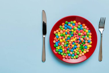 cutlery on table and sweet plate of candy. Health and obesity concept, top view on colored background.