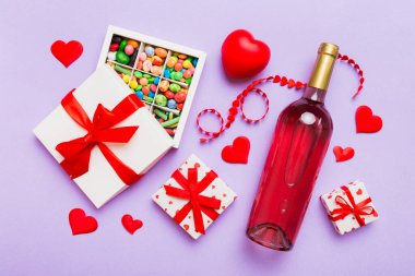 Sevgililer Günü için renkli arka planda bir şişe kırmızı şarap hediye ve çikolatalı. Kalp, hediye kutusuyla şekillendirilmiş çikolatalar fotokopi alanı ile üst görünüm.