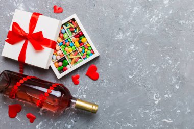 Sevgililer Günü için renkli arka planda bir şişe kırmızı şarap hediye ve çikolatalı. Kalp, hediye kutusuyla şekillendirilmiş çikolatalar fotokopi alanı ile üst görünüm.