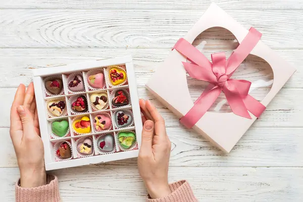 Female hands with delicious candies in box on color background.