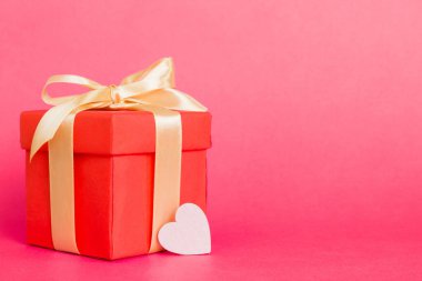 gift box with red bow and red heart on colored background. Perspective view. Flat lay.