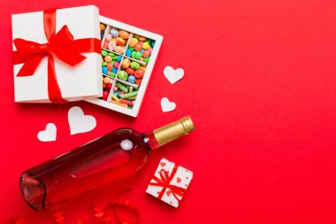 Sevgililer Günü için renkli arka planda bir şişe kırmızı şarap hediye ve çikolatalı. Kalp, hediye kutusuyla şekillendirilmiş çikolatalar fotokopi alanı ile üst görünüm.