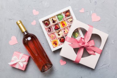 Sevgililer Günü için renkli arka planda bir şişe kırmızı şarap hediye ve çikolatalı. Kalp, hediye kutusuyla şekillendirilmiş çikolatalar fotokopi alanı ile üst görünüm.