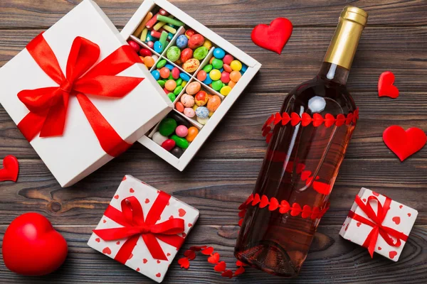 Bottle of red wine on colored background for Valentine Day with gift and chocolate. Heart shaped with gift box of chocolates top view with copy space.