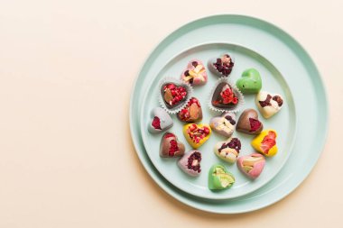 Plate with different chocolate on colored background. Assortment of fine chocolates top view vith copy space Health and obesity concept.