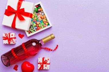 Sevgililer Günü için renkli arka planda bir şişe kırmızı şarap hediye ve çikolatalı. Kalp, hediye kutusuyla şekillendirilmiş çikolatalar fotokopi alanı ile üst görünüm.