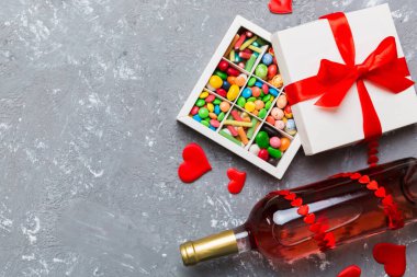 Sevgililer Günü için renkli arka planda bir şişe kırmızı şarap hediye ve çikolatalı. Kalp, hediye kutusuyla şekillendirilmiş çikolatalar fotokopi alanı ile üst görünüm.