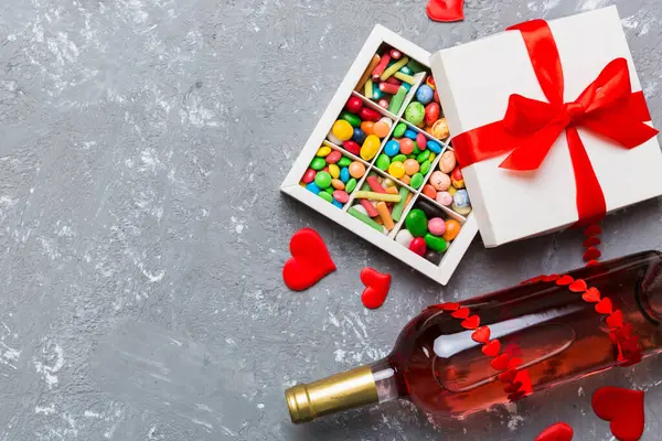 Sevgililer Günü için renkli arka planda bir şişe kırmızı şarap hediye ve çikolatalı. Kalp, hediye kutusuyla şekillendirilmiş çikolatalar fotokopi alanı ile üst görünüm.