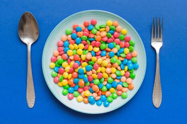 cutlery on table and sweet plate of candy. Health and obesity concept, top view on colored background.