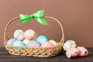 Mutlu Paskalya kompozisyonu. Renkli masada sarı laleli sepetli Paskalya yumurtaları. Fotokopi alanı olan doğal renkli yumurtalar.