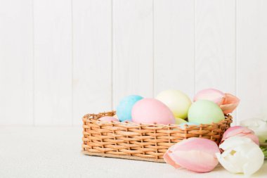 Mutlu Paskalya kompozisyonu. Renkli masada sarı laleli sepetli Paskalya yumurtaları. Fotokopi alanı olan doğal renkli yumurtalar.