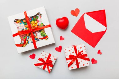 Red envelope with candy and gift box and Valentines hearts on colored background. Flat lay, top view. Romantic love letter for Holiday concept.