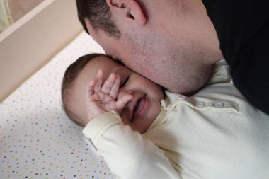 Mutlu baba ve oğul evde eğleniyor. Baba ve bebek yatak odasında, parlak bir arka planda. Şefkat, ebeveynlik.