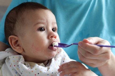 Yemek yiyen küçük bir çocuğun portresi. Yemek koltuğunda kaşığı olan bir bebek. Güzel bebek ilk yemeğini yiyor..