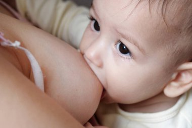 Genç bir kadın bebeğini evde emziriyor. Annenin göğsünden çıkan süt, bebek için doğal bir ilaçtır. Yeni doğan bebek bakıcılığıyla Anneler Günü bağ kurma kavramı.