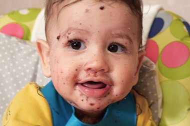 Yemek yiyen küçük bir çocuğun portresi. Yemek koltuğunda kaşığı olan bir bebek. Güzel bebek ilk yemeğini yiyor..