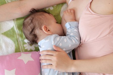 Genç bir kadın bebeğini evde emziriyor. Annenin göğsünden çıkan süt, bebek için doğal bir ilaçtır. Yeni doğan bebek bakıcılığıyla Anneler Günü bağ kurma kavramı.