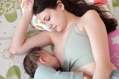 Genç bir kadın bebeğini evde emziriyor. Annenin göğsünden çıkan süt, bebek için doğal bir ilaçtır. Yeni doğan bebek bakıcılığıyla Anneler Günü bağ kurma kavramı.