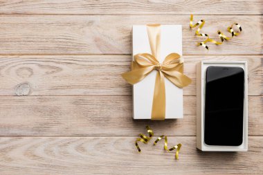 Altın kurdeleli hediye kutusu ve arka planda akıllı telefon, üst manzara. Boş kutu paketleme modeli, tasarımınız için şablon - markalaşma modeli.