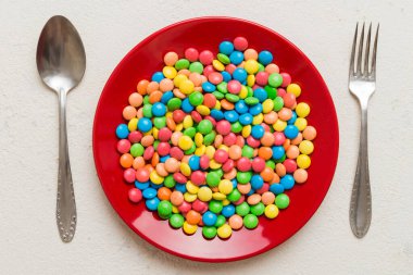 cutlery on table and sweet plate of candy. Health and obesity concept, top view on colored background.