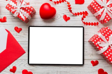 Top view of digital tablet with gift boxes and hearts on colorful background. Tablet with black screen with Holiday decorations gift box top view.