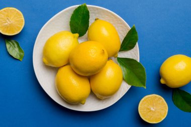 Taze kesilmiş limon ve tüm limonları renkli arka planda yuvarlak tabakta. Yemek ve içecek malzemeleri hazırlanıyor. Sağlıklı beslenme teması üst görünüm kopyalama alanı.