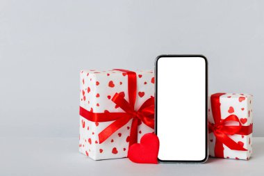 mobile phone with blank screen on colored background with hearts, calendar and gift box, valentine day concept perspertive view flat lay.