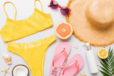 Yüzme havuzu aksesuarı konsepti. Masadaki plaj eşyalarının üst görüntüsü, parlak bikini, hasır şapka ve güneş kremi. Renkli plaj kıyafeti. Üst Görünüm Düz yatar, Boşluğu kopyala.